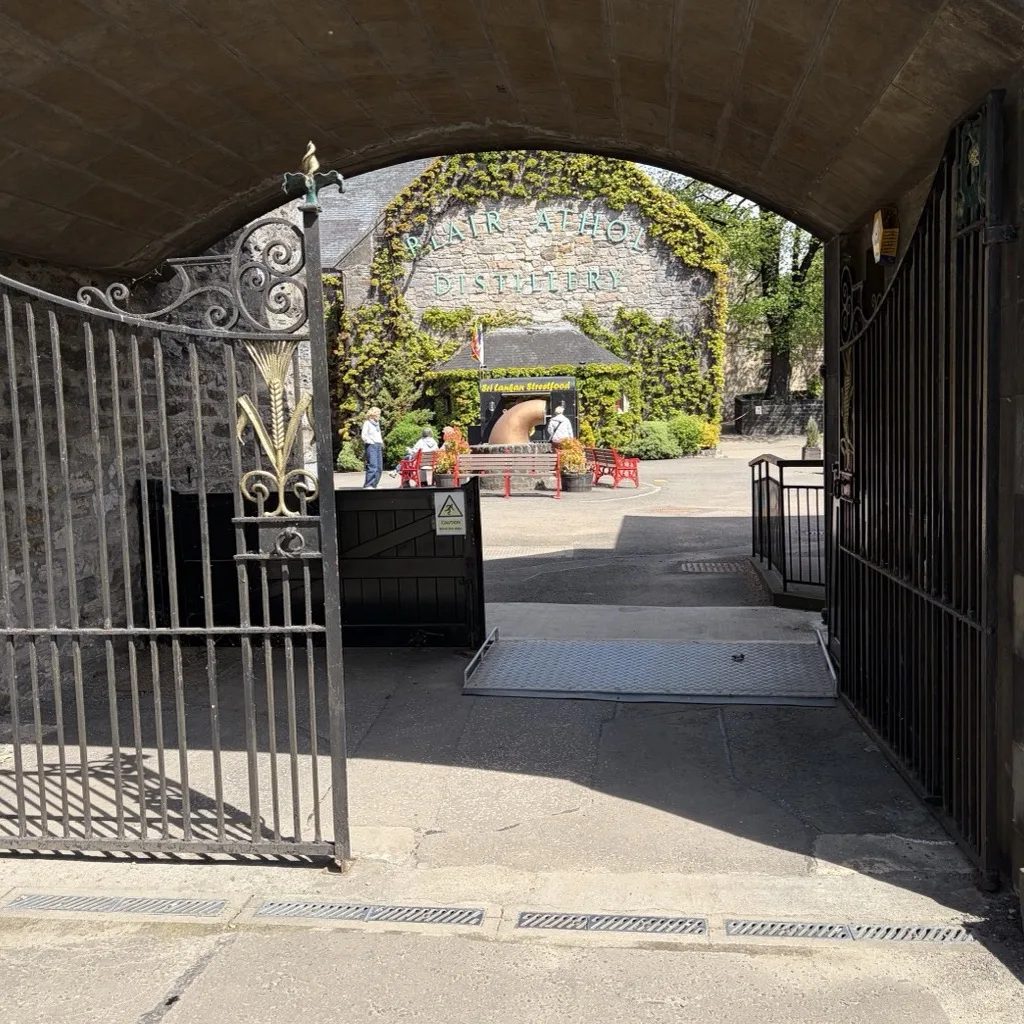 Blick durch den dunklen Torbogen auf den sonnigen, blühenden Innenhof von Blair Athol