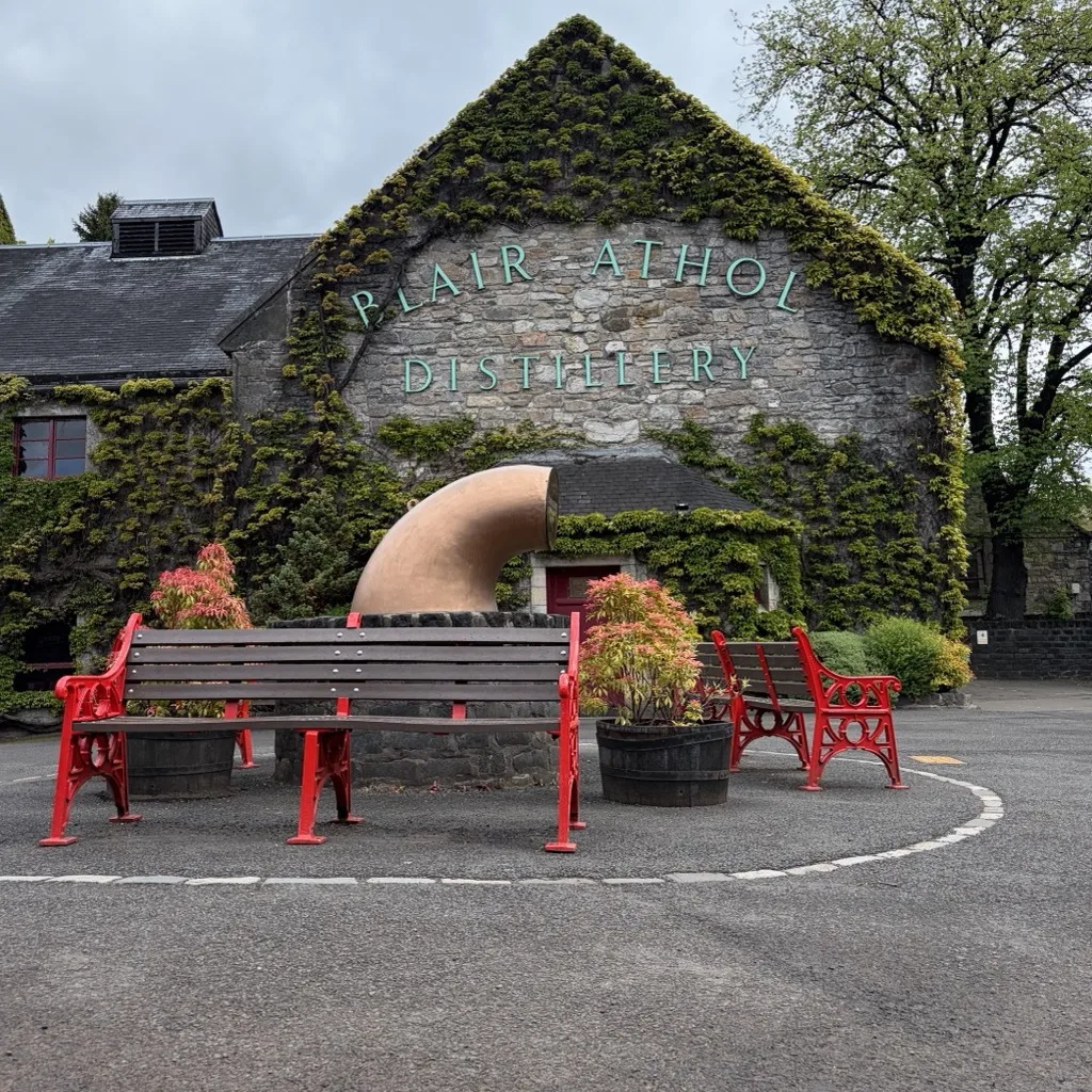 Der efeubewachsene Giebel der Blair Athol Distillery mit dem Schriftzug und roten Bänken davor